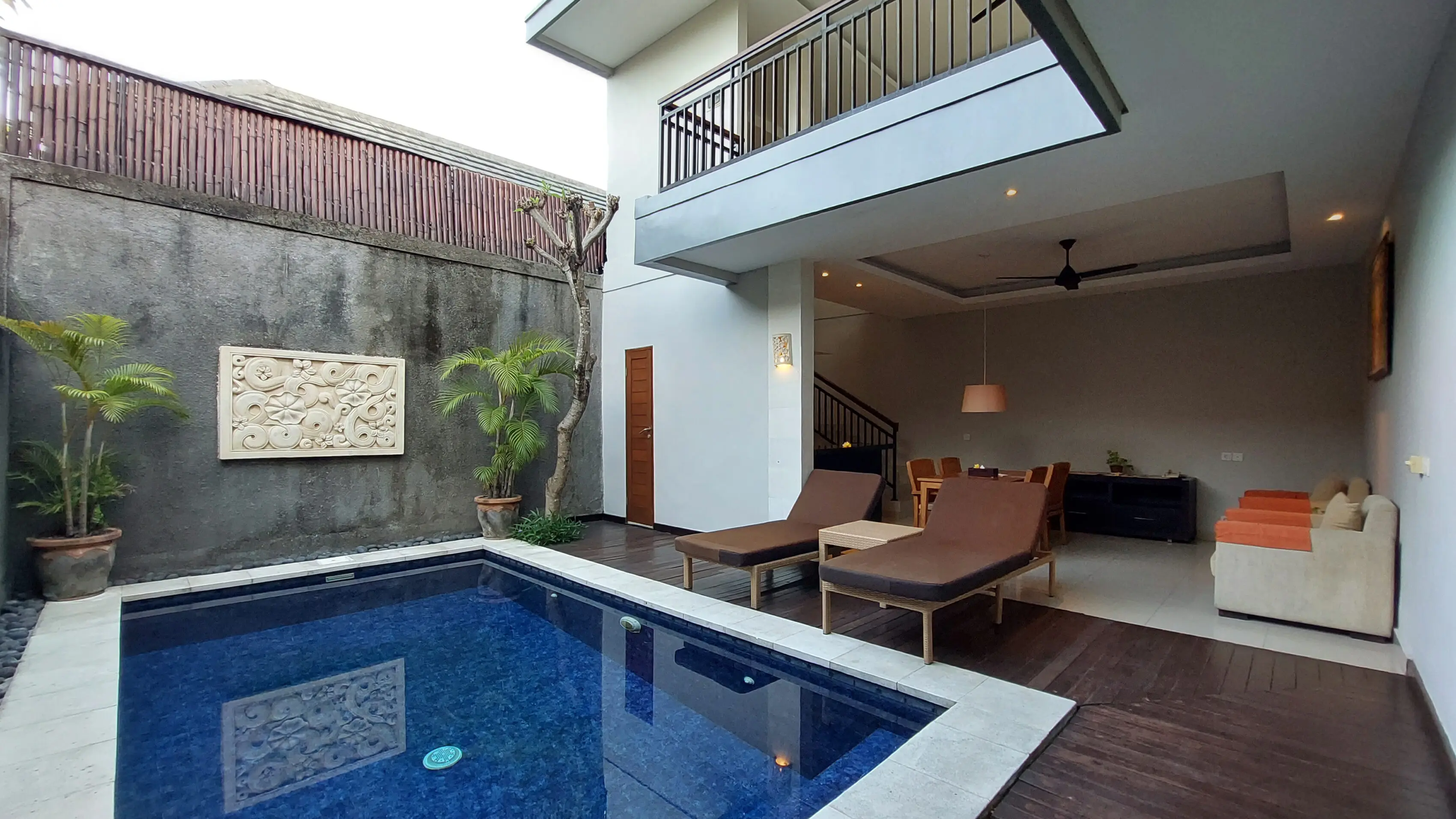 Two-bedroom villa pool deck with sun loungers, sandstone wall carving, balcony above and open living area on the right.