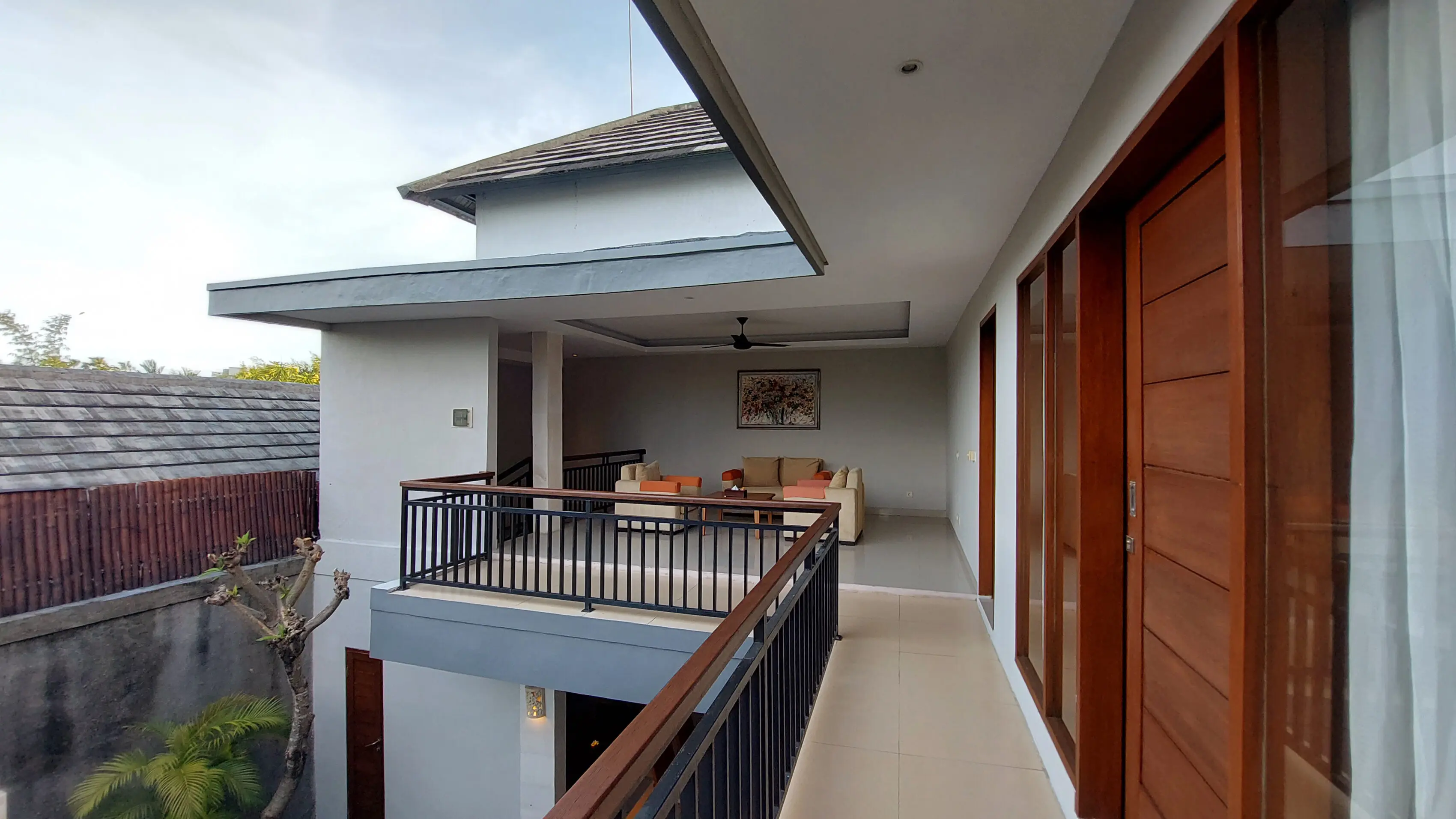 Upper-floor balcony walkway of the two-bedroom villa with a frangipani tree and view of the living area below.