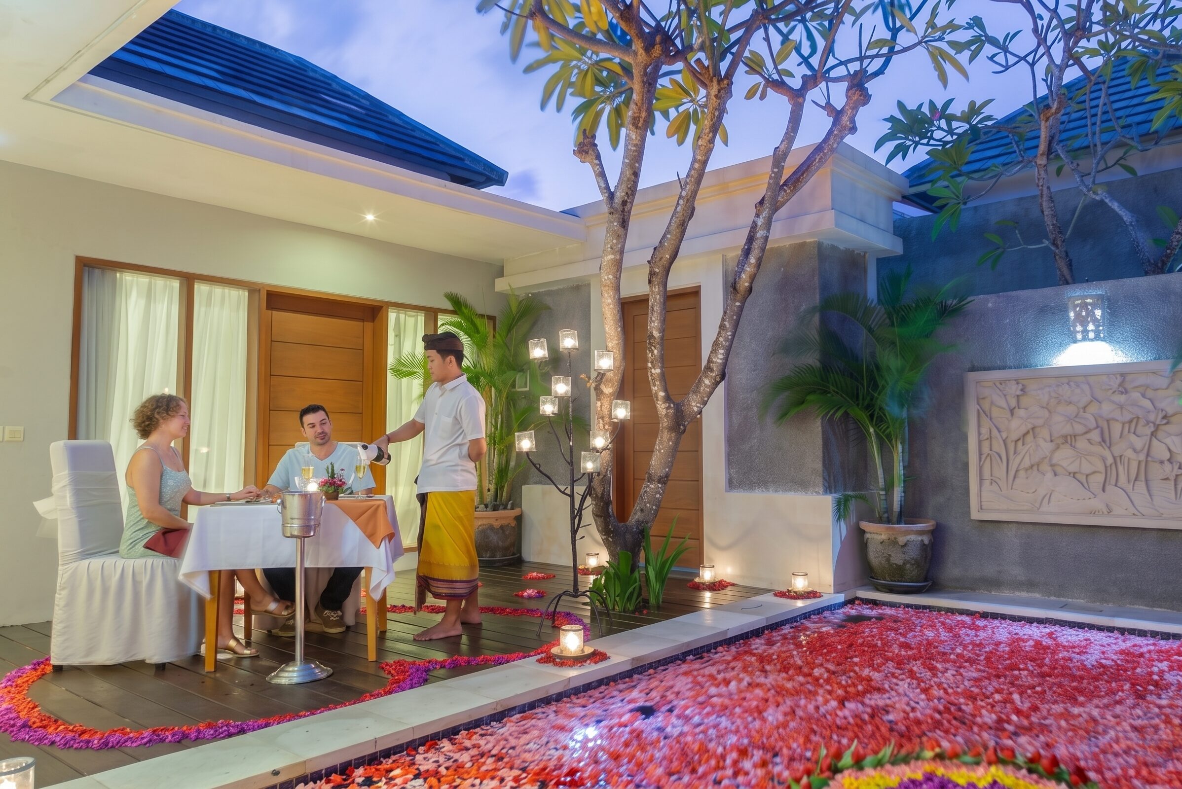 Romantic candlelit table set for two beside a pool decorated with rose petals at The Light Exclusive Villas & Spa.