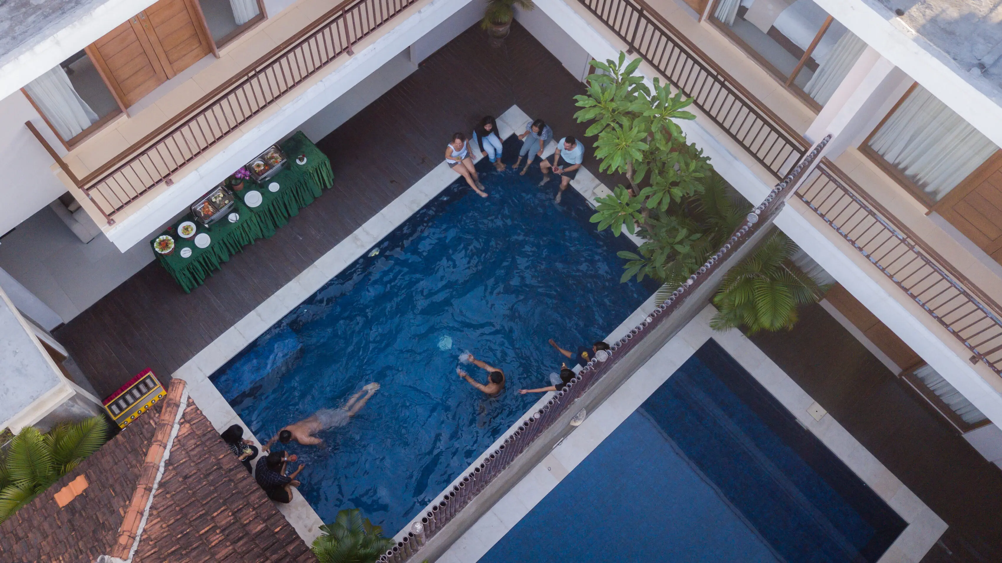 Top-down view of the four-bedroom villa's private courtyard pool with green-clad buffet table and guests around the edge.