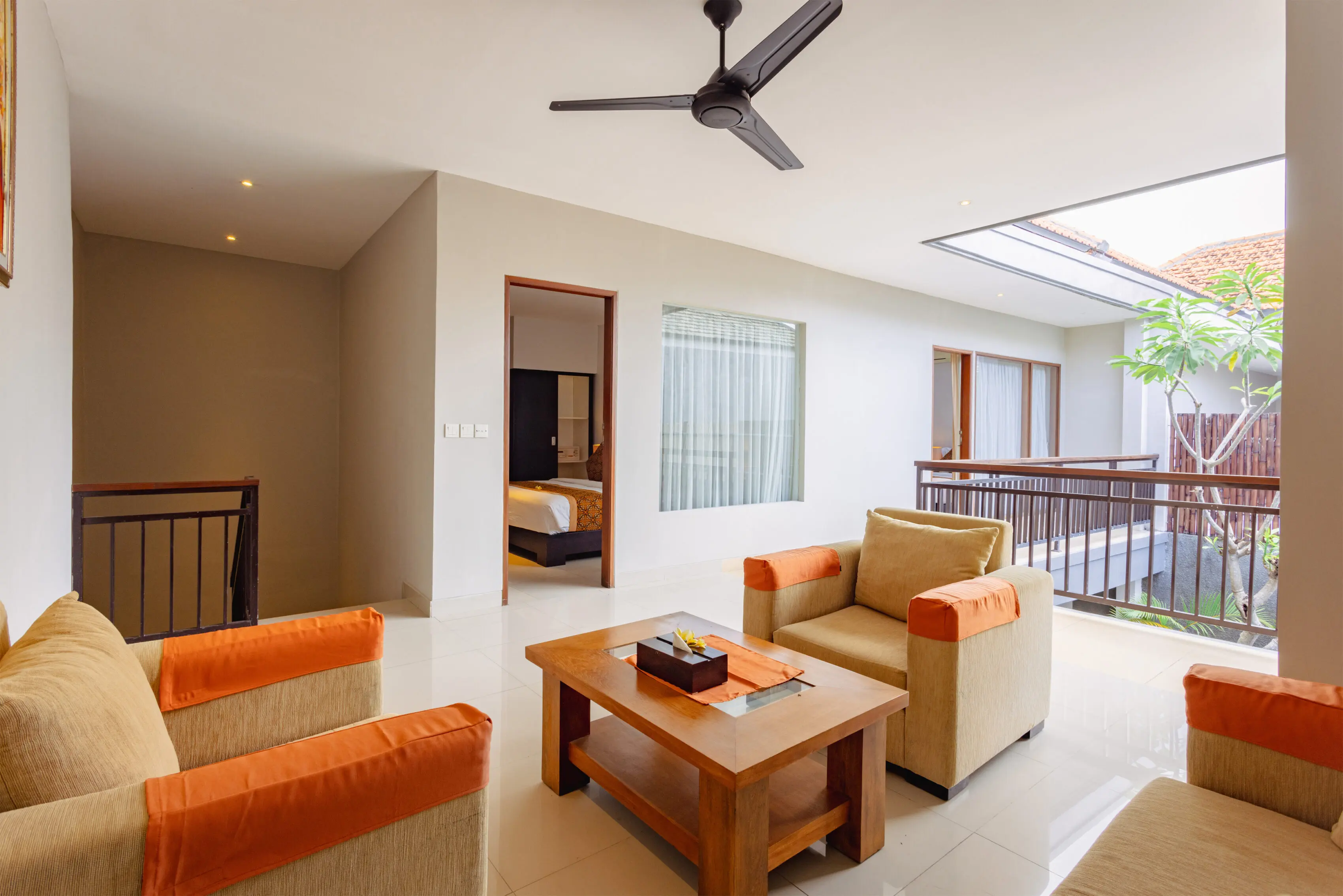 Four-bedroom villa bedroom with four-poster bed draped in white mosquito netting, orange batik cushions and pool view.