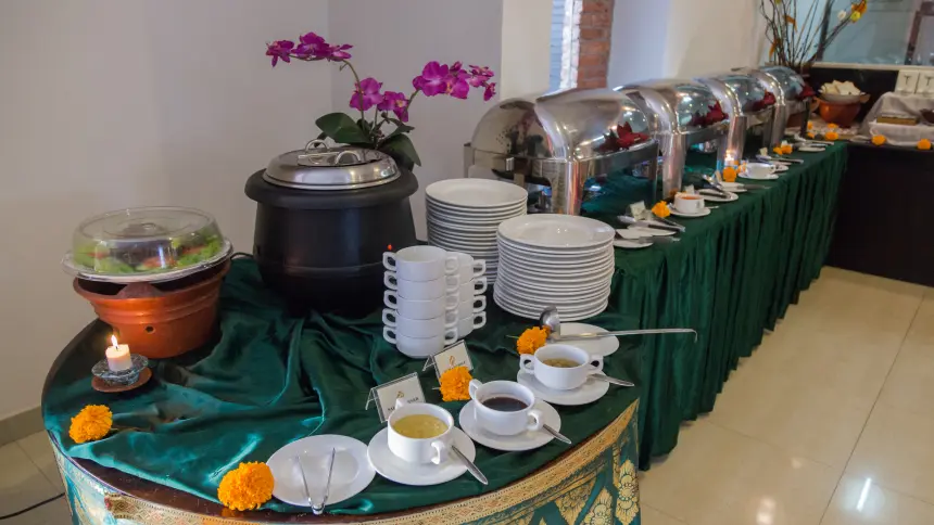Buffet table draped in green silk with chafing dishes, soup tureen, stacked plates, orchids and marigolds.