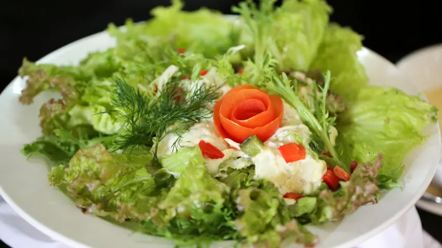 Fresh garden salad with mixed lettuce, dill, peppers and a carved tomato rose centrepiece on a white plate.