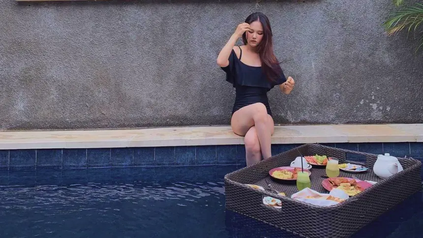 Floating breakfast next to a seated woman on the poolside at The Light Exclusive Villas & Spa, Seminyak, Bali.