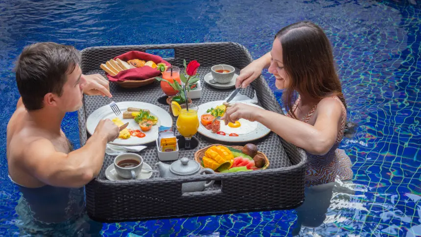 Couple enjoying a generous floating breakfast tray with eggs, mango, watermelon and juice in their private pool.