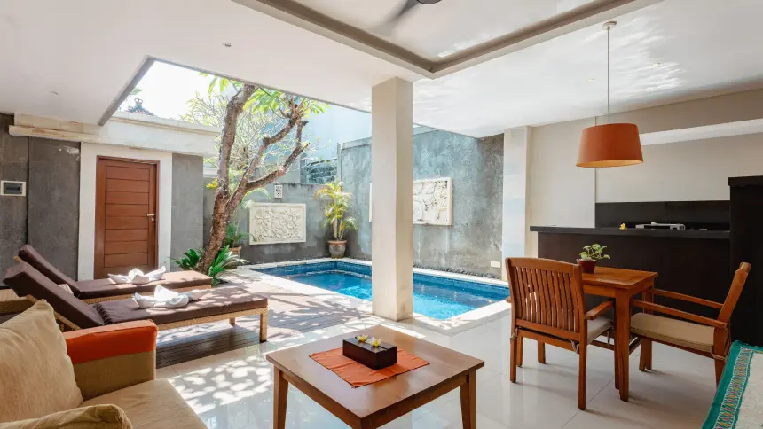 One-bedroom villa open living space with sun loungers, pillared central column, frangipani tree and small private pool.