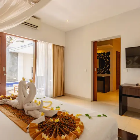 Master bedroom decorated with towel swans on the bed, batik runner and frangipani blossoms, with a glimpse of the private pool.