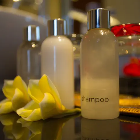 Bathroom amenity bottles — shampoo and conditioner — arranged with frangipani blooms on a polished countertop.