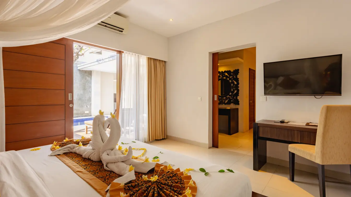 One-bedroom villa bedroom with four-poster canopy bed dressed with towel swans, frangipani petals and a private pool view.