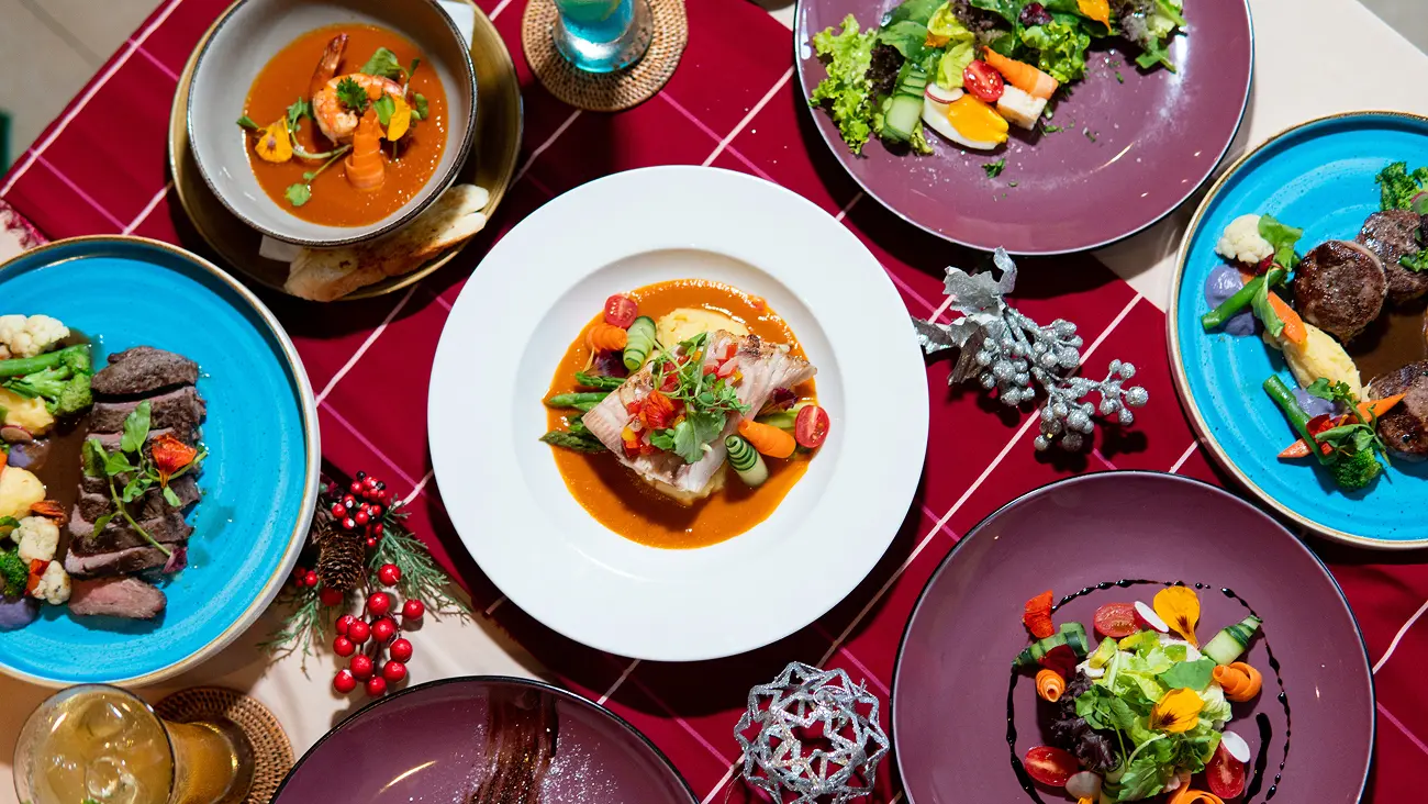 Romantic proposal dinner spread with steak, fish, soup and salad courses arranged on a red tablecloth.