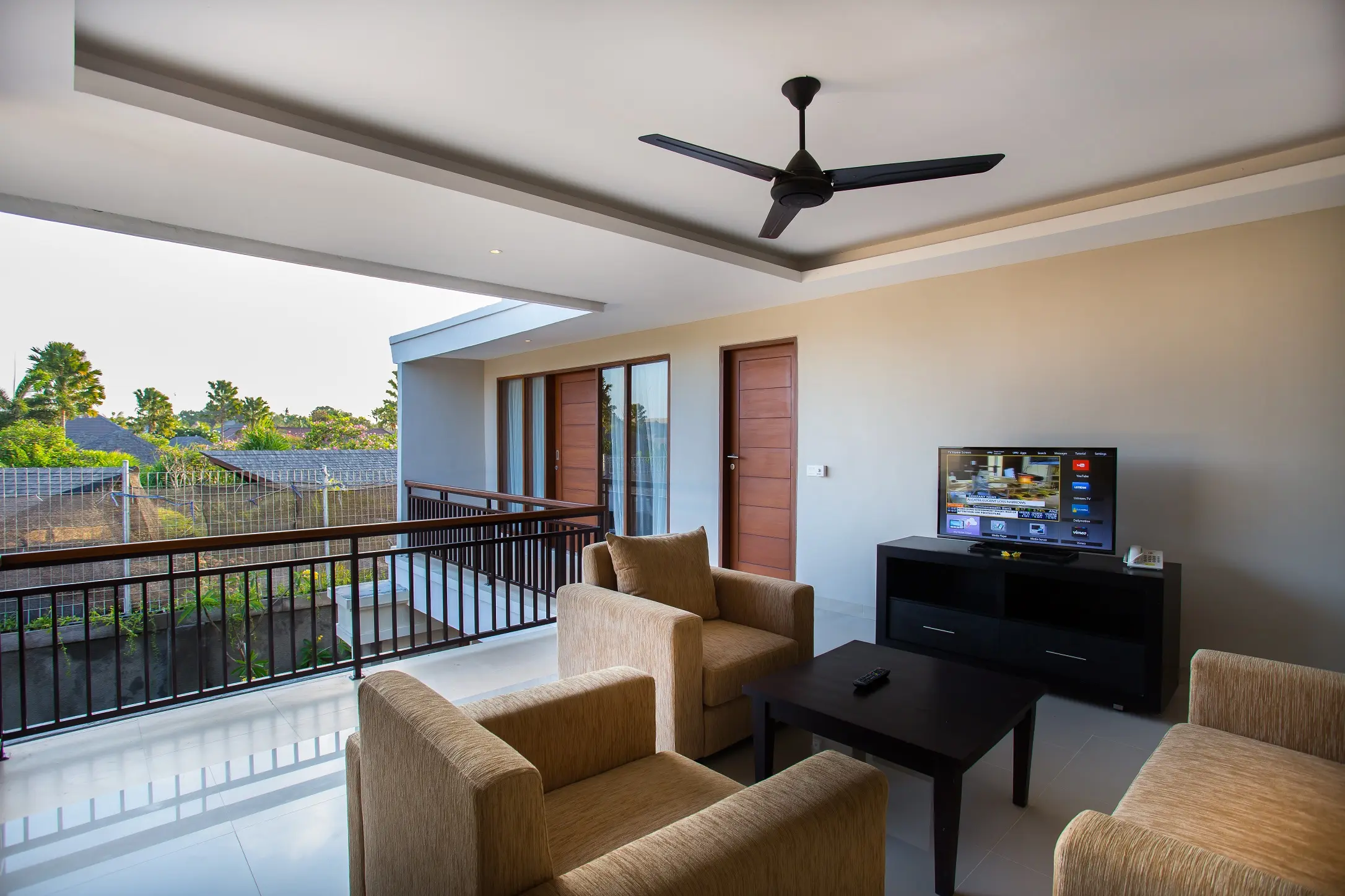 Upper-floor lounge of the two-bedroom villa with sofas, TV unit, ceiling fan and balcony view over the rice fields.