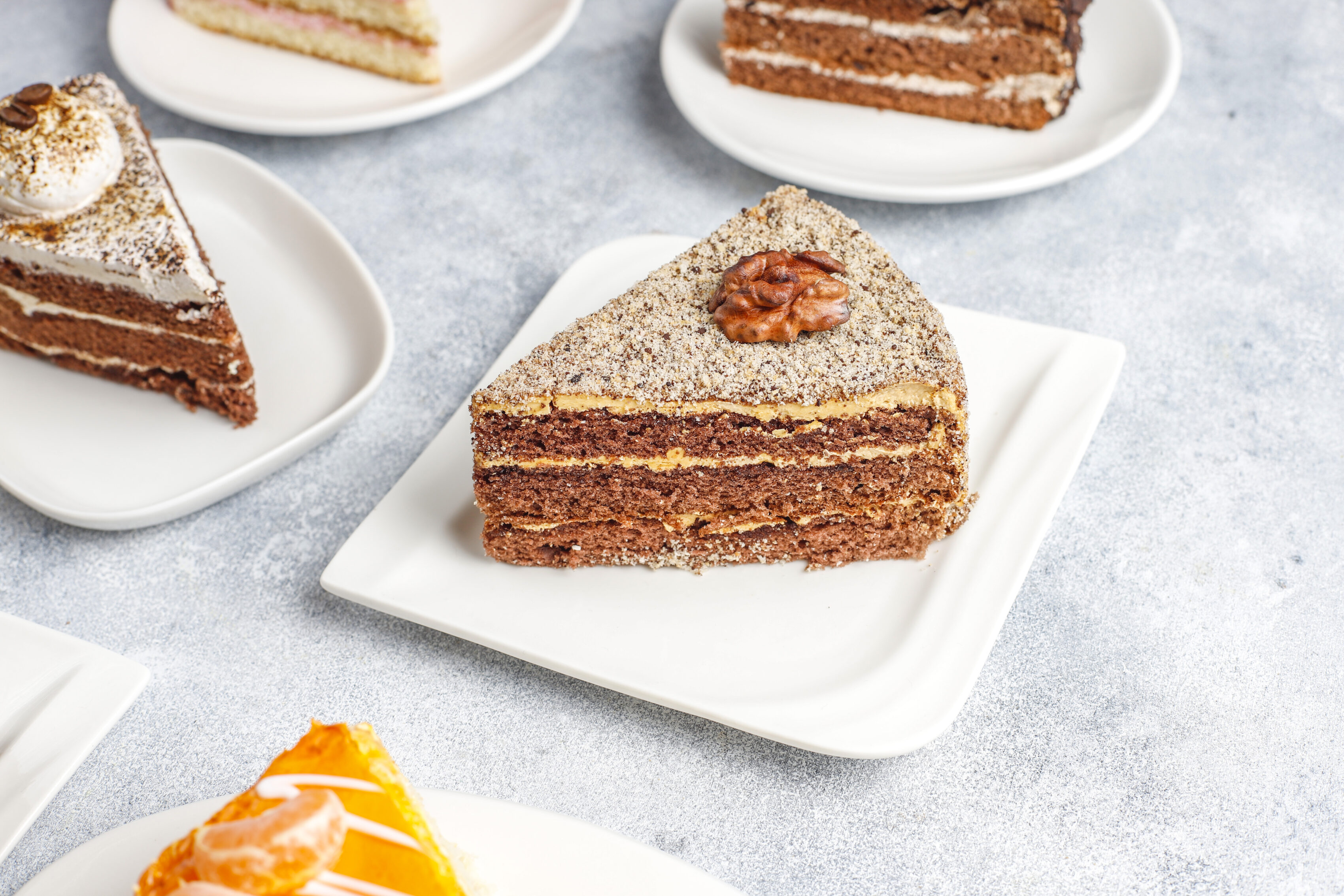 Assorted layered cake slices including a walnut-topped chocolate honey cake on small white plates.