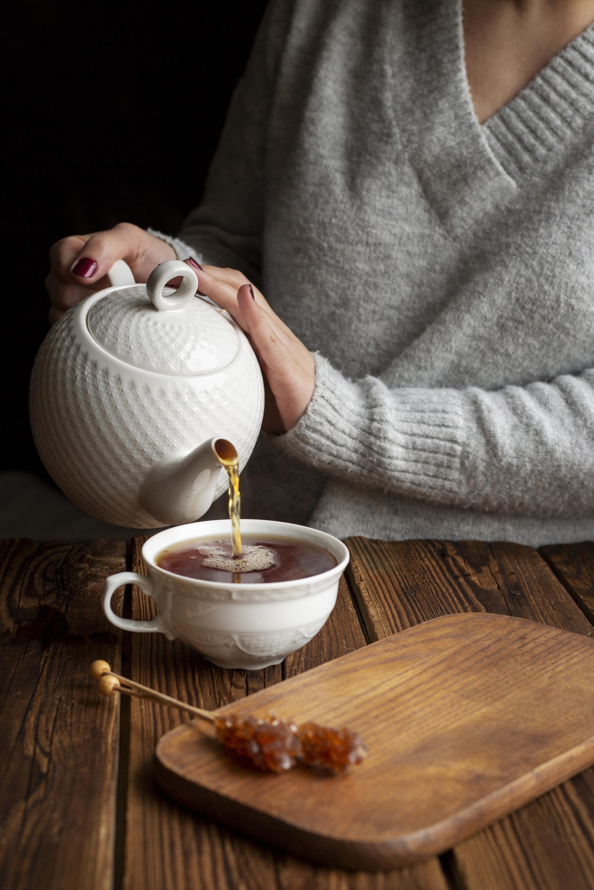 Pouring tea into a white cup on a wooden table with a cozy atmosphere, matched with sugar sticks for an elegant afternoon tea.