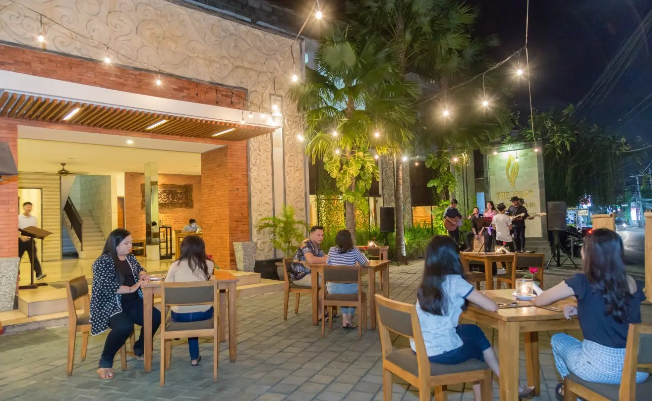 Couples dining at an outdoor restaurant terrace decorated with string lights, palms and live music in the background.