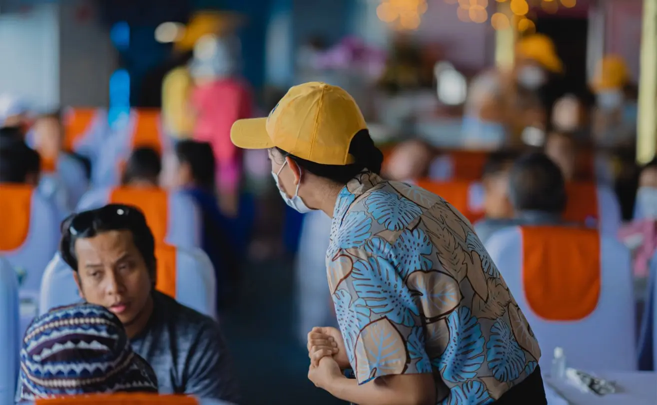 Server in floral shirt and yellow cap attends guests on a lively cruise dining experience.