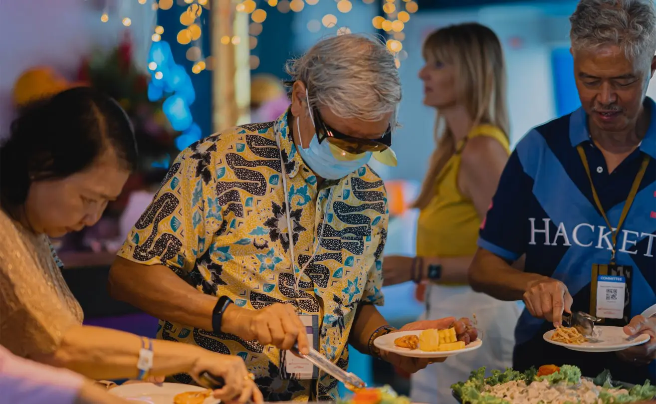 Guests enjoying a buffet with a variety of dishes at a vibrant social gathering, adorned with colorful lights.