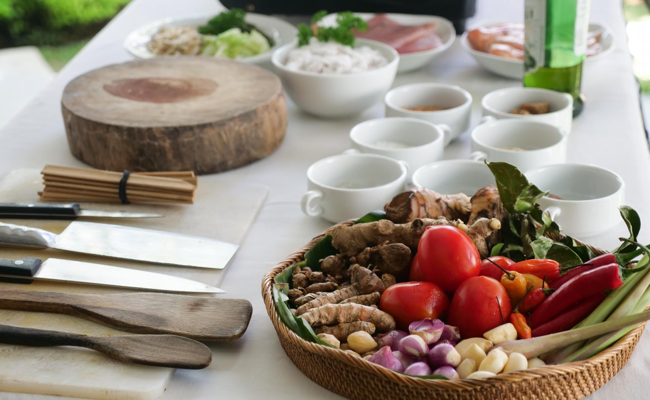 Fresh ingredients for a Balinese cooking at a table, featuring colorful herbs, spices, knives, and wooden utensils.