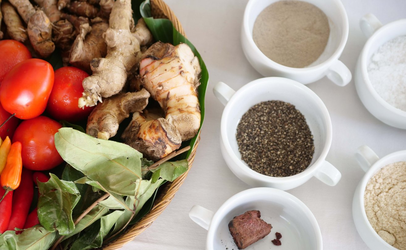 Fresh herbs and spices, including tomatoes, ginger, and chili peppers, arranged with small bowls of seasoning for Balinese cooking class.